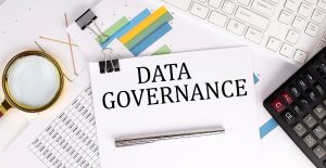 Paper labeled "Data Governance" on a desk with charts, a keyboard, a calculator, a pen, and a magnifying glass.